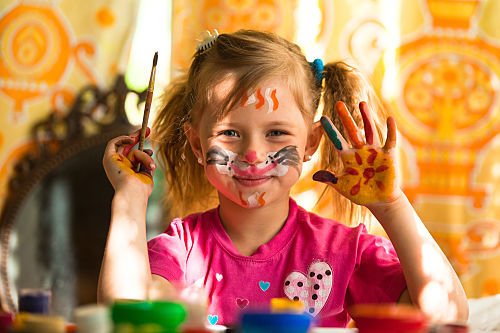young girl having fun with painting pictures on her face and hands