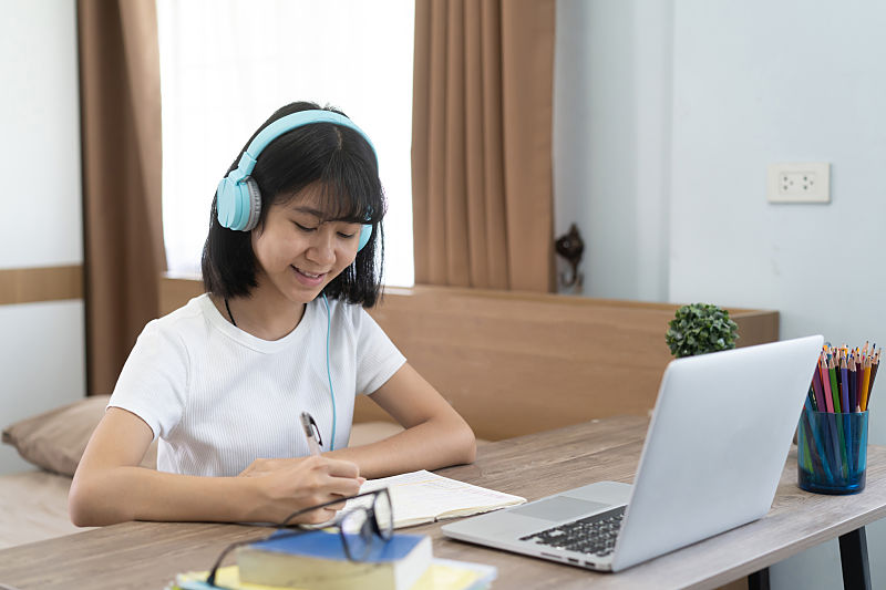 girl sitting at a table with laptop and headphone being tutored online